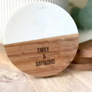 May include: A round, white marble and wood coaster with the names "Emily & Raymond" engraved on the wood.