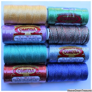 May include: An assortment of eight spools of metallic nylon thread in various colors, including gold, green, purple, and blue. Each spool is labeled "OMEGA" and "No. 3 - 180 m (196 yds.)". The thread is designed for fine and brilliant weaving.