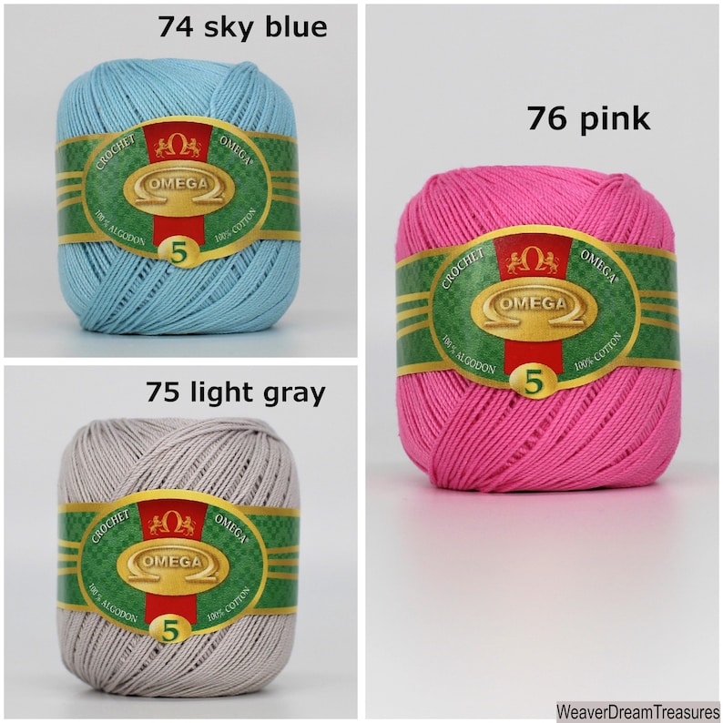 May include: Three balls of yarn in different colors: sky blue, light gray, and pink. Each ball has a label that says "Omega" and "100% Algodon" in green and gold lettering.