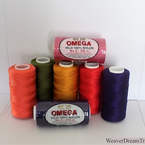 May include: Six spools of Omega brand 100% nylon thread in various colors, including orange, green, yellow, red, and purple. The spools are labeled "OMEGA HILO 100% NYLON No. 5 - 275 m PARA HAMACAS Y TEJDOS".