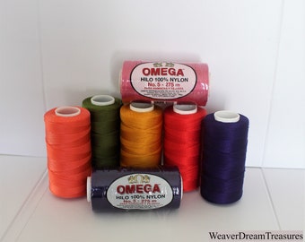 May include: Six spools of Omega brand 100% nylon thread in various colors, including orange, green, yellow, red, and purple. The spools are labeled "OMEGA HILO 100% NYLON No. 5 - 275 m PARA HAMACAS Y TEJDOS".