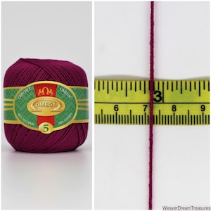 May include: A ball of deep purple crochet yarn with a green label that reads "CROCHET OMEGA 100% ALGODON 5 OMEGA 100% COTTON". A close-up of the yarn shows the thickness of the yarn next to a measuring tape.