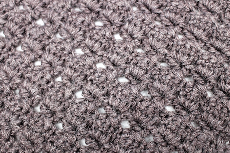 May include: Close-up of a crocheted fabric with a textured, open-weave pattern. The fabric is a dark brown color.