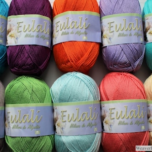 May include: Ten balls of yarn in various colors, including teal, purple, orange, lavender, light blue, green, coral, and beige. Each ball has a label that reads "Eulali Hilos de Algodon".