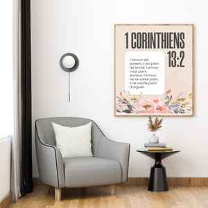 May include: A framed print with the text "1 CORINTHIANS 13:2" and a floral design. The print hangs above a gray armchair with a white pillow. A small black side table and a decorative wall lamp are also visible.