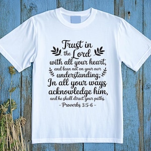 May include: White t-shirt with the text "Trust in the Lord with all your heart, and lean not on your own understanding; In all your ways acknowledge him, and he shall direct your paths. - Proverbs 3:5-6-" in black script.