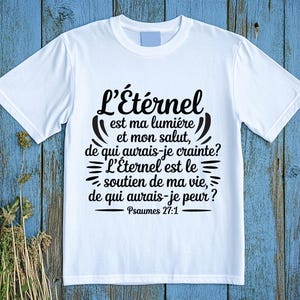 以下が含まれることがあります： フランス語の黒いテキストが入った白いTシャツ。「L'Éternel est ma lumière et mon salut, de qui aurais-je crainte? L'Éternel est le soutien de ma vie, de qui aurais-je peur?」詩篇27:1と書かれています。