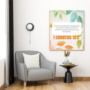 Peut inclure: Une impression encadrée avec le texte "El amor es paciente, es benigno; el amor no tiene envidia; el amor no es jactancioso, no se envanece. 1 CORINTIOS 13:2" est accrochée au-dessus d'un fauteuil gris avec un coussin blanc. Une petite table d'appoint noire et une horloge murale sont également visibles.