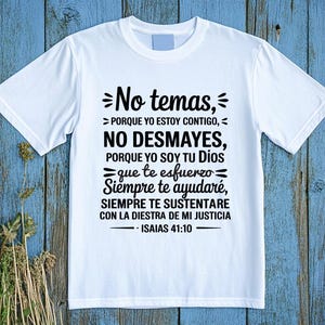 May include: White t-shirt with black text in Spanish. The text includes the phrases "No temas, No desmayes" and a Bible verse from Isaiah 41:10. The shirt is displayed on a blue wooden surface.