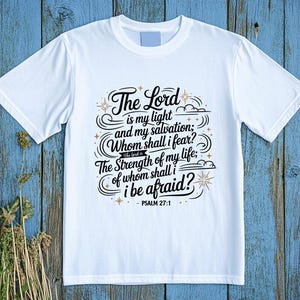 May include: White t-shirt with the text "The Lord is my light and my salvation; Whom shall I fear? The Strength of my life; of whom shall I be afraid?" in a decorative script. The text is from Psalm 27:1.