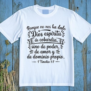 May include: White t-shirt with black text in Spanish. The text reads "Porque no nos ha dado Dios espíritu de cobardía, sino de poder, de amor y de dominio propio. 1 Timoteo 1:7". The shirt is on a blue wooden surface.