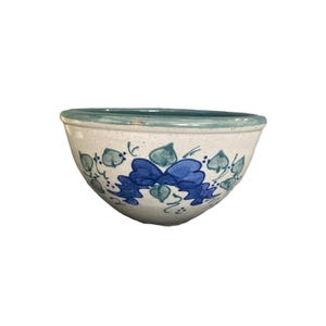 May include: A ceramic bowl with a speckled off-white base, featuring a hand-painted design of blue bows and green leaves. The rim is painted in a solid teal color, and the interior of the bowl is finished in a matching teal glaze.