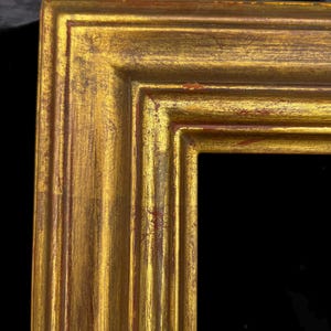 May include: A rectangular picture frame featuring a metallic gold finish with visible red undertones and distressed textures. The frame has a multi-tiered, stepped profile with clean mitered corners and a deep, recessed inner edge.