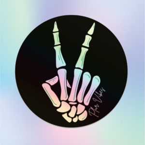 May include: A black circle sticker with a rainbow skeleton hand making the peace sign. The text "Good Vibes" is written in a script font on the sticker.