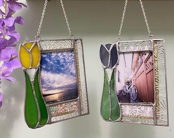 May include: Two rectangular stained glass photo frames hanging from silver chains. The left frame features a yellow tulip accent with a sunset photo. The right frame features a dark blue tulip accent with a bicycle photo. Both have textured glass borders.