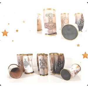 May include: Set of six drinking horns with various Norse-inspired designs, including a hammer, a knot, and a circle. The horns are made of natural materials and have a polished finish. The horns are displayed on a white surface with a gold rim.