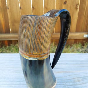 May include: A dark brown and black drinking horn with a wooden base and a carved wooden band around the top. The horn has a dark brown handle.