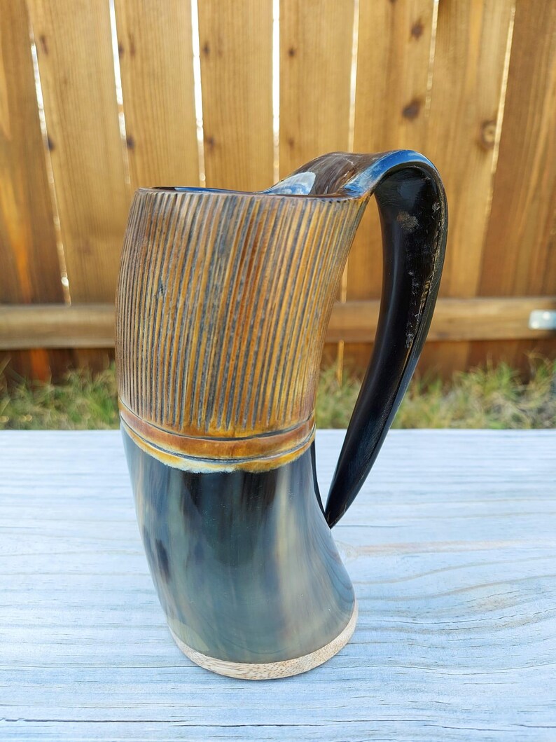 May include: A dark brown and black drinking horn with a wooden base and a carved wooden band around the top. The horn has a dark brown handle.