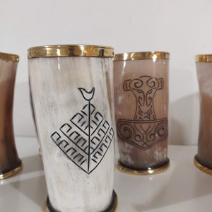 May include: Set of four drinking horns with gold rims and black etched designs. The designs include a tree, a hammer, and a geometric pattern.