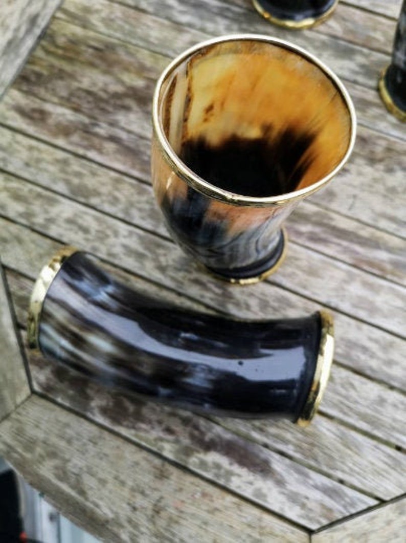 May include: Two drinking horns with gold trim. One horn is upright and the other is lying down. Both horns are made of dark brown and black material.