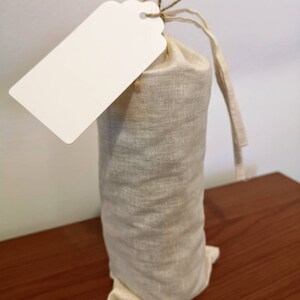 May include: A white gift tag with a brown string attached to a beige linen drawstring bag.