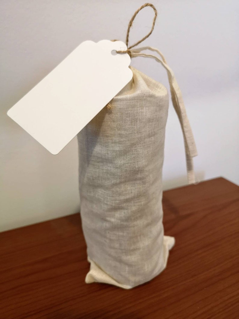 May include: A white gift tag with a brown string attached to a beige linen drawstring bag.