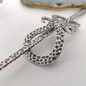May include: Silver hair stick with a hammered finish and a decorative swirl design.