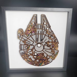 Może przedstawiać: Drewniana dekoracja ścienna przedstawiająca szczegółową sylwetkę statku kosmicznego Millennium Falcon z Gwiezdnych Wojen, ozdobiona kwiatowymi wzorami w odcieniach różowego, zielonego i brązowego.