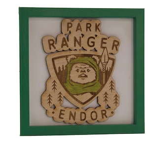 May include: A wooden sign with a green frame, featuring a cartoon character with a green hood and the text "Park Ranger Endor".