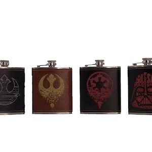 May include: Four stainless steel hip flasks with different Star Wars designs. The flasks are black with brown leather accents. The designs include the Rebel Alliance symbol, the Imperial symbol, Darth Vader's helmet, and a quote from Darth Vader.