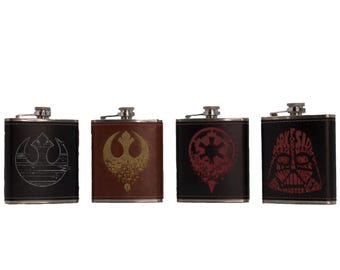Könnte beinhalten: Vier Edelstahl-Schnapsflaschen mit verschiedenen Star Wars-Designs. Die Flaschen sind schwarz mit braunen Lederakzenten. Die Designs beinhalten das Symbol der Rebellenallianz, das imperiale Symbol, Darth Vaders Helm und ein Zitat von Darth Vader.