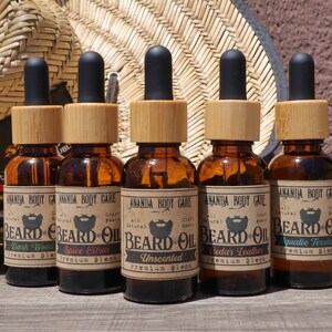 May include: Six amber glass bottles with bamboo lids and black droppers filled with beard oil. The bottles are labeled with the text "Amanda Body Care" and "Beard Oil" with different scents: "Dark Wood", "Spice Citrus", "Unscented", "Cedar Leather", and "Aquatic Territory".