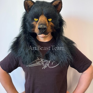 May include: A realistic bear head mask featuring thick black faux fur, a brown muzzle, and piercing yellow eyes. The mask includes a black nose and visible teeth. The text Art Beast Team is printed across the chest of the dark brown t-shirt.