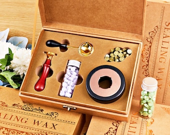 May include: A brown box set containing sealing wax supplies. Includes a red-handled wax stamp, a gold-colored melting spoon, a black and copper wax warmer, and two small glass bottles filled with wax beads. The box is labeled "SEALING WAX".