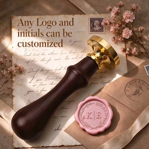 May include: A wax seal stamp with a dark brown wooden handle and a gold-toned metal head. Beside it lies a round, light pink wax seal featuring the initials KE, a floral wreath design, and the date 330.07.26. Text reads: Any Logo and initials can be customized.