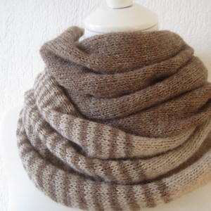 Op de afbeelding: Een gestreepte gebreide sjaal in bruin en beige. De sjaal is gevouwen en wordt getoond op een wit mannequin.