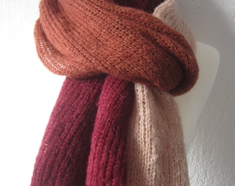 May include: A long, knitted scarf in three colors: rust, burgundy, and blush pink. The scarf is folded and draped over a white mannequin.