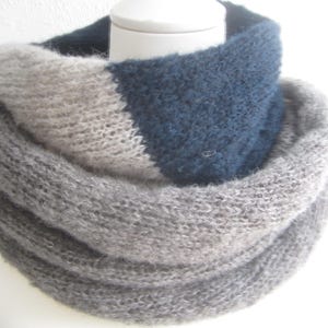 Peut inclure: Une écharpe infinie en tricot épais présentant un design color-block avec des sections bleu marine foncé, beige clair et gris chiné. L'accessoire possède une texture douce et duveteuse, disposé en plusieurs boucles circulaires autour d'un support.