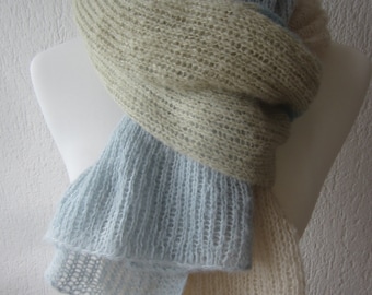 May include: A long, knitted scarf featuring a color-blocked design in soft shades of pale blue, beige, and cream. The scarf has a loose, airy, and semi-sheer texture with a visible ribbed knit pattern, draped around a white mannequin torso.