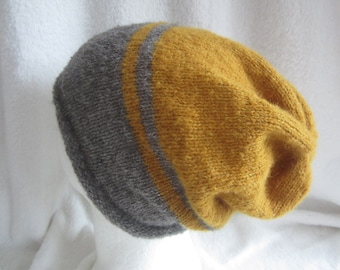 May include: A knitted beanie featuring a color-blocked design with a large section of mustard yellow and a smaller section of charcoal gray, separated by a thin gray stripe. The hat has a soft, fuzzy texture and a slouchy, relaxed fit.