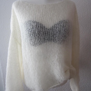 Könnte beinhalten: Ein cremefarbener, locker gestrickter Pullover mit weitem Ausschnitt und langen Ärmeln. Der Pullover hat ein transparentes, offen gestricktes Design, das ein dunkel gefärbtes Unterkleid freigibt. Der Gesamtstil ist lässig und bequem.