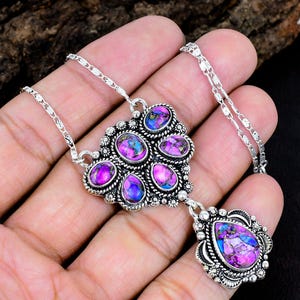 May include: A silver necklace featuring a cluster of six oval-shaped purple and blue stones set in ornate metal frames. The pendant includes a larger pear-shaped stone drop at the bottom, all connected by a delicate silver chain with textured links.