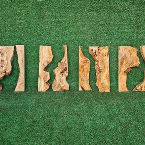 May include: Five pieces of wood with natural wood grain and unique shapes. The wood is light brown with darker brown streaks. The pieces are arranged in a row on a green surface.