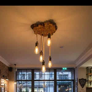 May include: Interior shot of a cafe with a rustic aesthetic. Features a long wooden table with benches, exposed brick walls, and a unique light fixture made from a tree trunk. Large windows offer a view of the outside.