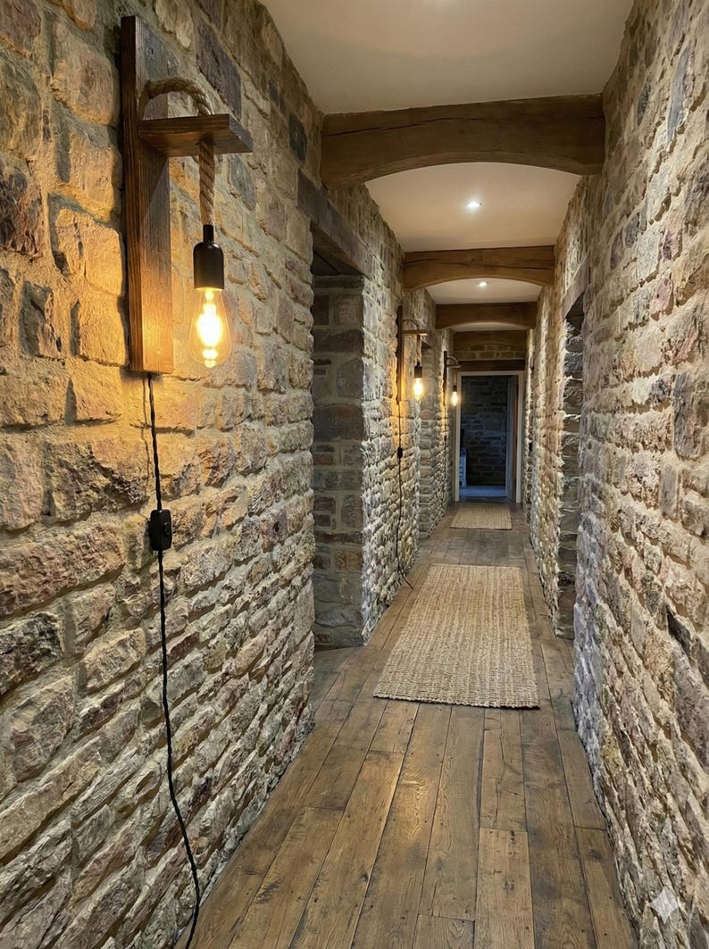May include: A wall-mounted light fixture featuring a dark wood rectangular backplate, a horizontal wooden shelf, and a thick rope cord suspending a black socket with an Edison-style light bulb. The fixture includes a black power cord and switch.