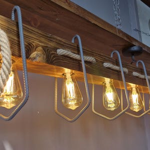 Puede incluir: Una l&aacute;mpara de techo de madera r&uacute;stica con ocho bombillas de filamento expuestas. La l&aacute;mpara est&aacute; hecha de madera recuperada y presenta detalles de cuerda. Las bombillas est&aacute;n encerradas en jaulas met&aacute;licas.