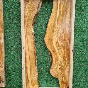 Puede incluir: Una losa de madera natural con un patr&oacute;n de veta &uacute;nico y fluido. La losa est&aacute; enmarcada en un marco de madera claro y mide 60 x 30 cm. La madera es de color marr&oacute;n claro con vetas marrones m&aacute;s oscuras.