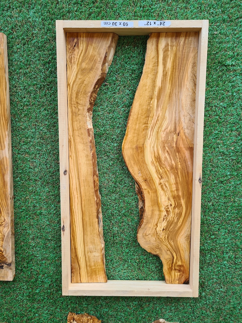 Puede incluir: Una losa de madera natural con un patr&oacute;n de veta &uacute;nico y fluido. La losa est&aacute; enmarcada en un marco de madera claro y mide 60 x 30 cm. La madera es de color marr&oacute;n claro con vetas marrones m&aacute;s oscuras.