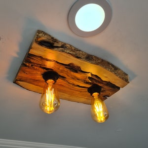 May include: A wooden ceiling light fixture with two Edison bulbs. The wood is a natural, light brown color with dark brown streaks. The fixture is mounted to the ceiling with two black metal brackets.