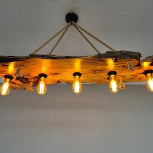 May include: A rustic wooden chandelier with six Edison-style light bulbs. The light fixture is suspended from the ceiling by thick rope. The wooden beam has a natural, rough edge and a warm, amber glow.